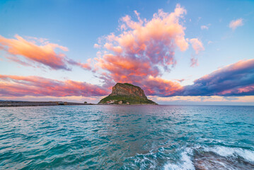Dramatic sunset illuminating Monemvasia and its rocky coastline in Greece. The sky above is bursting with vibrant colors as the sun sets over the mediterranean sea