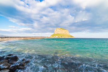Dramatic sunset illuminating Monemvasia and its rocky coastline in Greece. The sky above is bursting with vibrant colors as the sun sets over the mediterranean sea