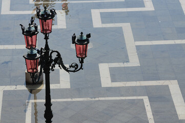 Pigeons on street lamps reflect on a wet Venetian plaza.
