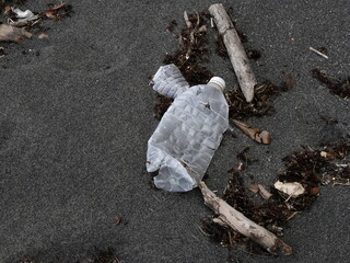used plastic water bottle on black sand beach. Plastic pollution in the ocean, drifting to the beach. Guadeloupe. Trash on the beach