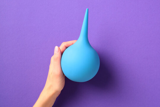 Blue rubber enema bulb in female hand against a purple background. Ideal for medical, health, or hygiene themes