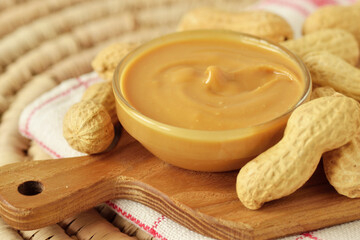 Peanut butter in glass bowl on wooden cutting board with peanuts