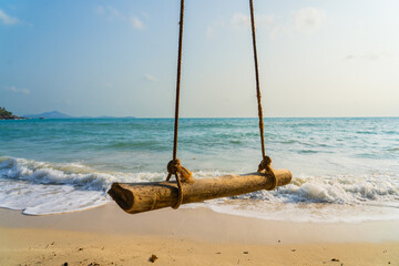 A rustic wooden swing hanging over gentle beach waves in a serene coastal setting during golden hour