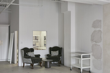 This modern, minimalist studio features two comfortable armchairs with patterned cushions, perfect for relaxing or holding small meetings. A rolling utility cart provides additional workspace