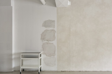 This modern, minimalist studio features a white rolling cart positioned in front of a textured wall with exposed patches. The contrast between the smooth cart and the rough wall