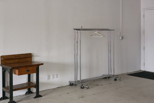 This modern, minimalist studio features a white garment rack on wheels, perfect for hanging clothes or displaying merchandise. A wooden workbench with drawers provides a functional workspace. The spac - Powered by Adobe