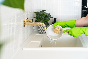 Person wearing green gloves washes a bowl on kitchen