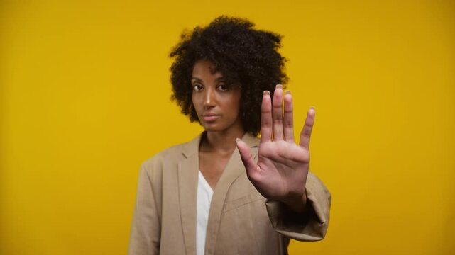 Confident Woman Showing Stop Gesture Against Yellow Background