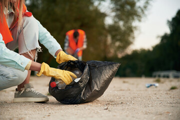 Picking up the bottle. A volunteers collects garbage on a muddy beach