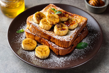 A stack of french toast topped with caramelized bananas and powdered sugar