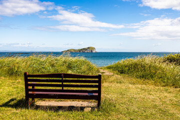 Serene Beachside Bench, bringing Solitude by the Sea through an empty bench with a view of Craigleith Island, North Berwick on a sunny day, Scotland, UK, 2024-29-06: