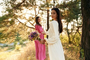 Naklejka premium Woman is want to go, with bouquet of flowers. Lovely lesbian couple are together outdoors in nature