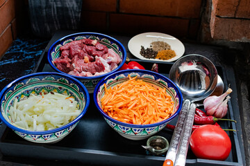 Meat and vegetables are cut for cooking plov. Plates with national ornaments on the table.