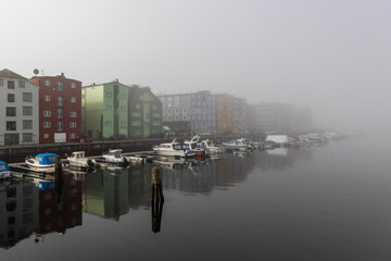 Häuser mit bunter Fassade am Hafen von Trondheim verschwinden im Herbstnebel 