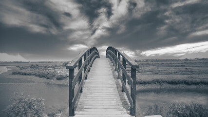 a grayscale shot of a wooden bridge over the lake in the countryside