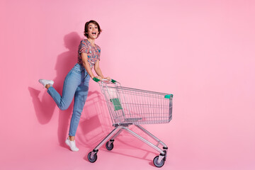 Photo of charming lovely excited girl wear stylish clothes push cart isolated on pink color...