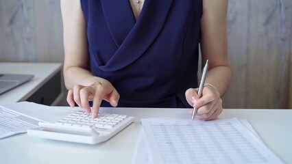 Businesswoman with dark blue dress is using white calculator and taking notes in her office. Taxes and audit in business
