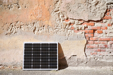 Photovoltaic solar panel at weathered, textured wall with peeling paint. Juxtaposition of modern...