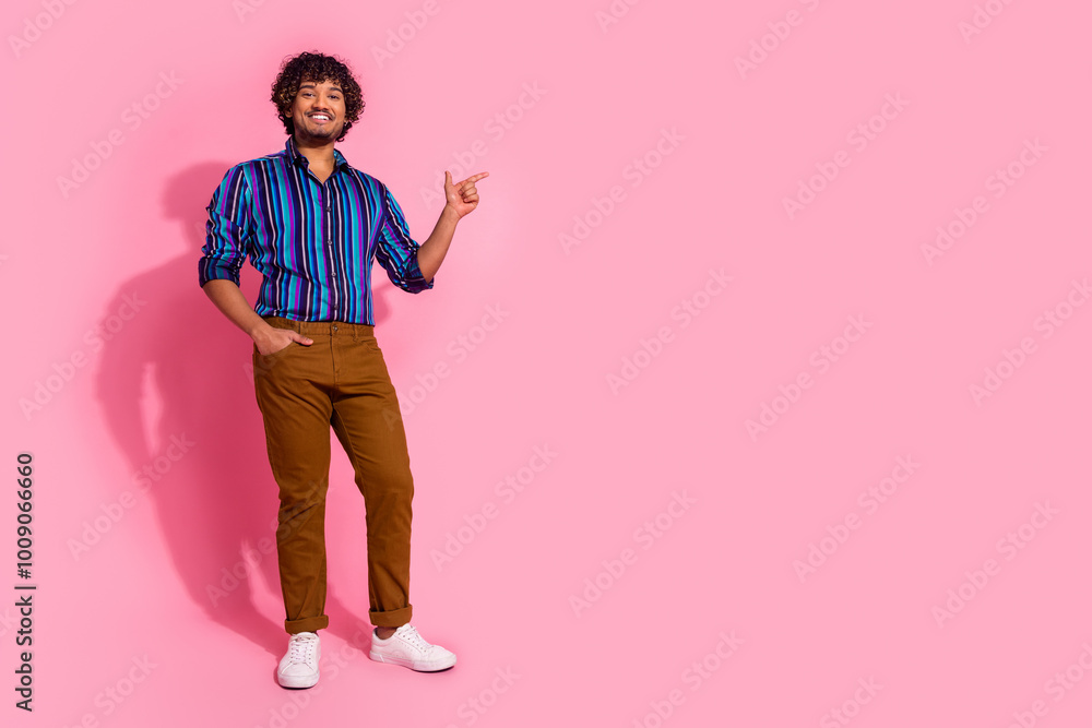 Poster Photo of nice cheerful man wear trendy striped clothes presenting empty space isolated on pink color background