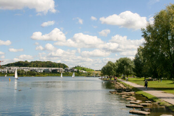 Phoenix See, Dortmund, Germany. Sunny summer day with blue skies, boats in the lake, people walking, swans in the water and hill in a background. Horizontal