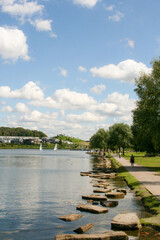 Fototapeta premium Phoenix See, Dortmund, Germany. Sunny summer day with blue skies, boats in the lake, people walking, swans in the water and hill in a background. Vertical