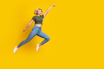 Obraz premium Full size photo of lovely girl dressed khaki crop top jeans fly raising fist up look empty space isolated on yellow color background