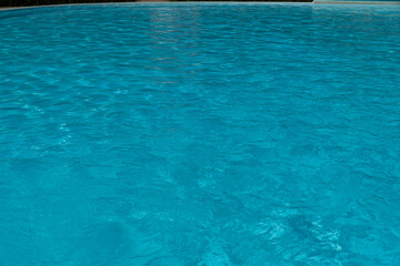 Sky blue water in a swimming pool with light reflections. Sunlight refraction on clear turquoise surface of a swimming pool. Relaxing transparent flowing water. Caustic turquoise pattern.