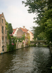 Historic buildings next to a canal with a stone bridge in the background in Bruges, Belgium