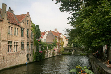 Obraz premium Historic buildings next to a canal with a stone bridge in the background in Bruges, Belgium