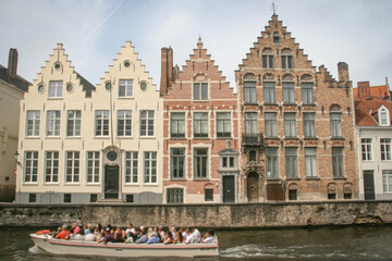 Naklejka premium A boat with tourists passing tall historic residential buildings next to a canal in Bruges, Belgium