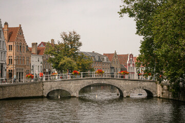 Historic stone bridge with red flowers over a canal in Bruges, Belgium, horizontal
