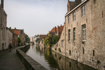 Tiny street with a canal and historic building on the side in Bruges, Belgium