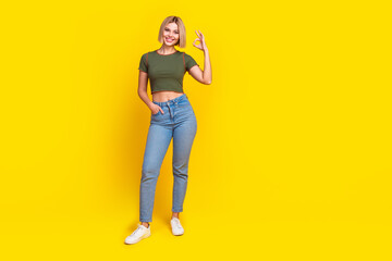 Full length photo of cheerful satisfied girl dressed khaki t-shirt jeans arm in pocket show okey isolated on yellow color background