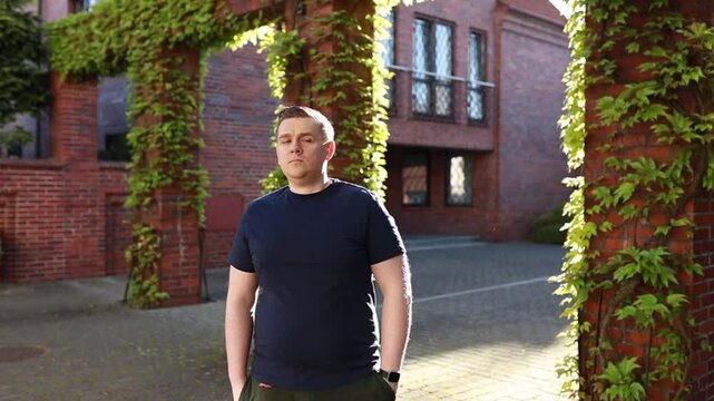 Stressed middle-aged age chubby overweight obese male inpatient, angry and anxious checking on a watch while standing on old European red bricks wall background on sunset, unhappy turning around