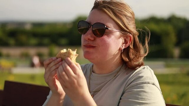 White woman eating sandwich on sunset, golden hour, epic summer scene, picnic, sun glasses on face, enjoyed woman's face, summer vibes, sunset in park, peaceful outdoor meal, overweight, chubby woman