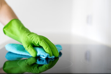 Hand in green glove cleaning a electric stove top with a blue cloth