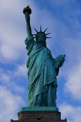 Fototapeta premium Vertikale, frontale Ansicht der berühmten Freiheitsstatue von New York, die vor klarem blauen Himmel die Fackel der Freiheit in die Luft streckt