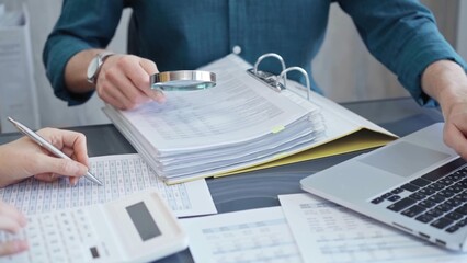 Business colleagues reviewing financial documents and calculating taxes. Auditor inspecting financial reports with magnifying glass. Business audit, taxes and forensic accounting concept