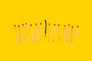 Wooden matches sticks, one burned on a yellow background with copy space