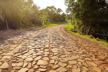 Road in a rural area made of irregular stones, with an orange hue at sunrise.
