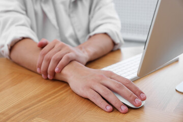 Man suffering from pain in wrist while working on computer at table indoors, closeup. Carpal tunnel syndrome