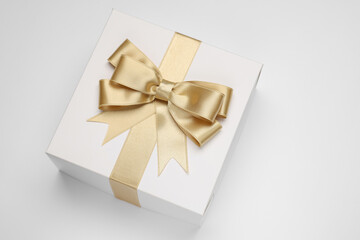 Gift box with golden bow on light grey background, above view