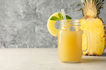 Tasty pineapple juice in mason jar, mint and slice of fresh fruit on grey textured table, closeup....