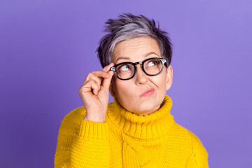 Thoughtful woman with glasses wearing a yellow sweater on a purple background