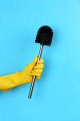 Woman holding black toilet brush on light blue background, closeup. Cleaning tool