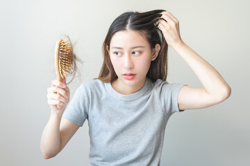 Serious asian young woman holding brush holding comb, hairbrush with fall black hair from scalp after brushing, looking on hand worry about balding. Health care, beauty treatment, hair loss problem.