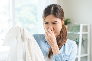 Asian young housewife woman having bad smelling clothes hand holding breath nose with finger, sniff...