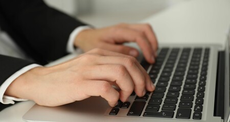 Businesswoman using laptop at white table indoors, closeup. Modern technology