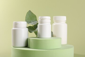 Plastic medical bottles, leaves and podiums on green background, closeup