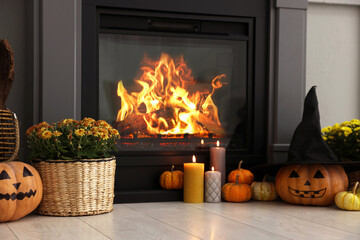 Pumpkins, burning candles and flowers near fireplace indoors. Halloween celebration